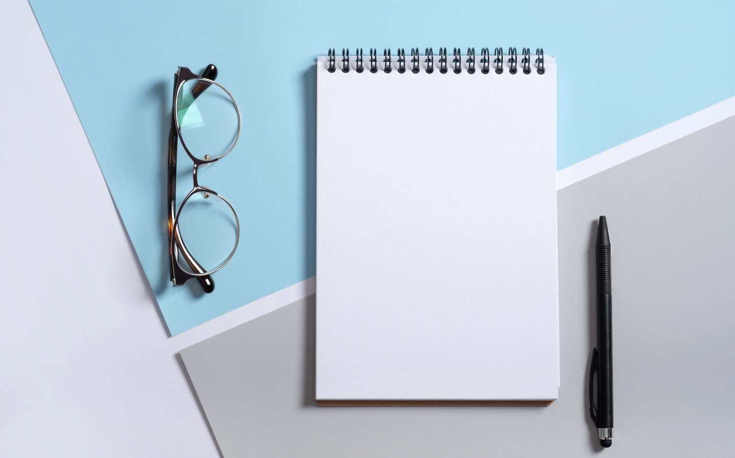 Notebook, pen and glasses arranged for stationery design